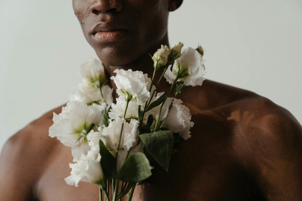 Artistic close-up of a shirtless man holding lisianthus blooms, capturing natural elegance.