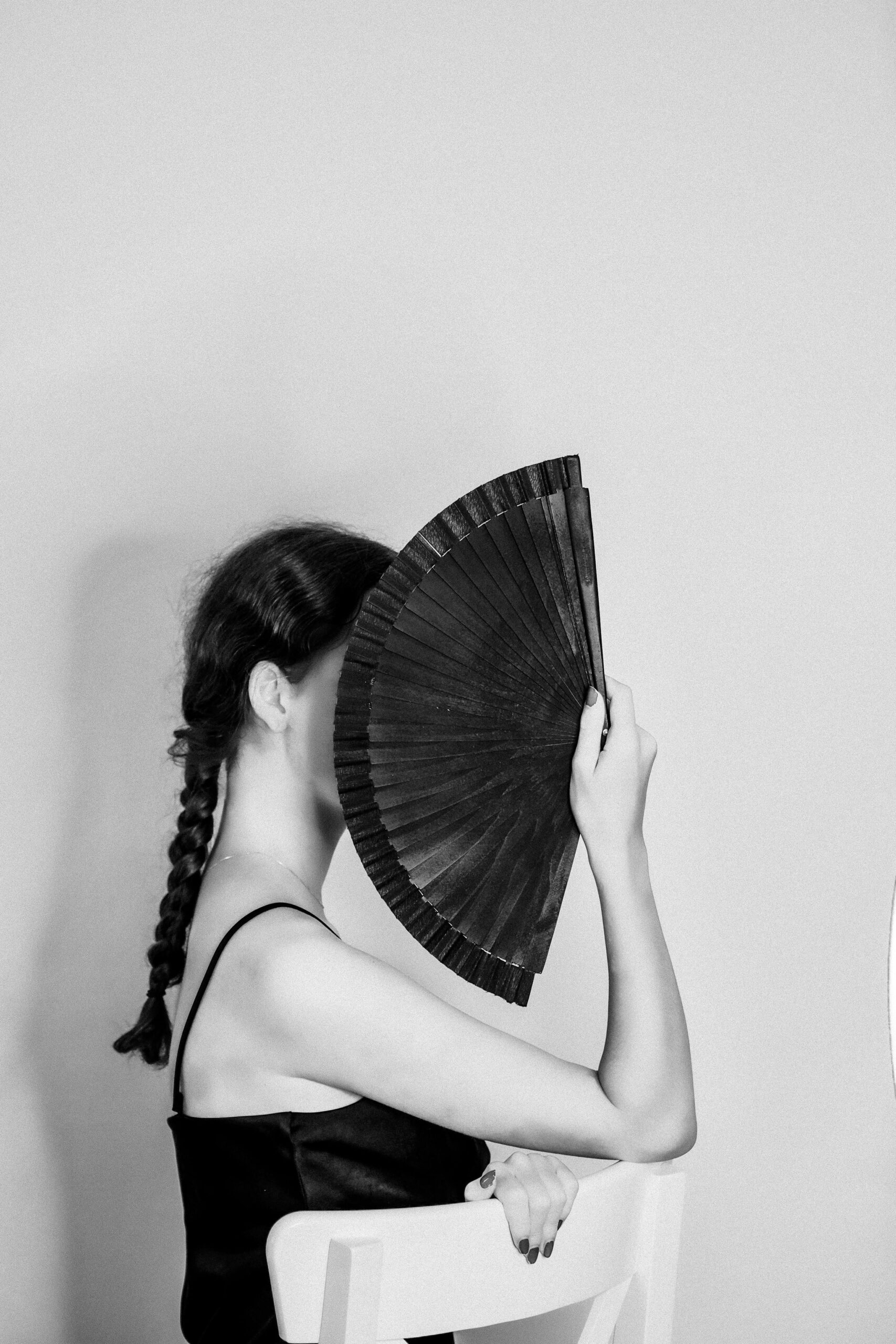 Black and white portrait of a woman posing with a hand fan, creating an artistic and elegant silhouette.